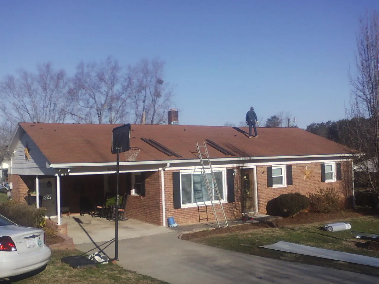 Roofer stripping a shingle roof on a brick ranch before metal panels in Pavilion