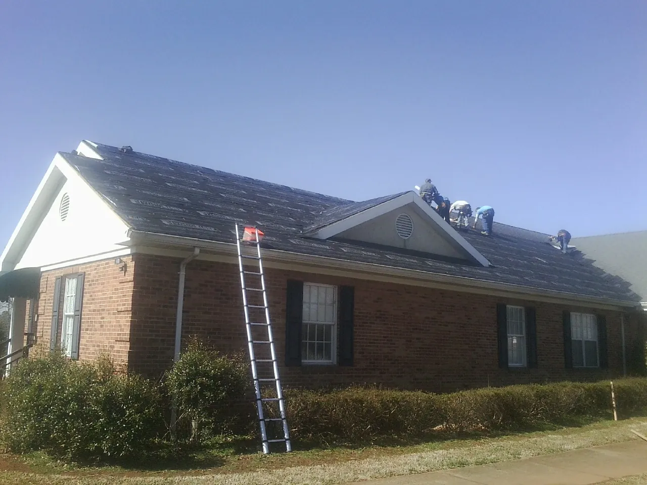 Crew tearing shingles off a brick ranch roof with a ladder set — Metal Roof Repair work by our crew in Pavilion