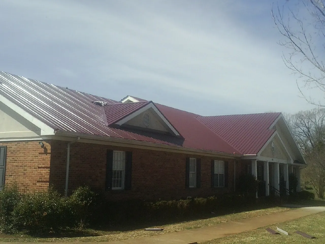 Red metal roof with gabled entries on a long brick building, from a Hail Damage Roof Repair job in Pavilion
