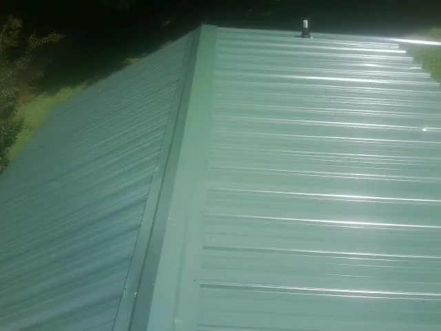 New green metal panels meeting at the ridge of a roof — Flat Roof Repair work by our crew in Pavilion