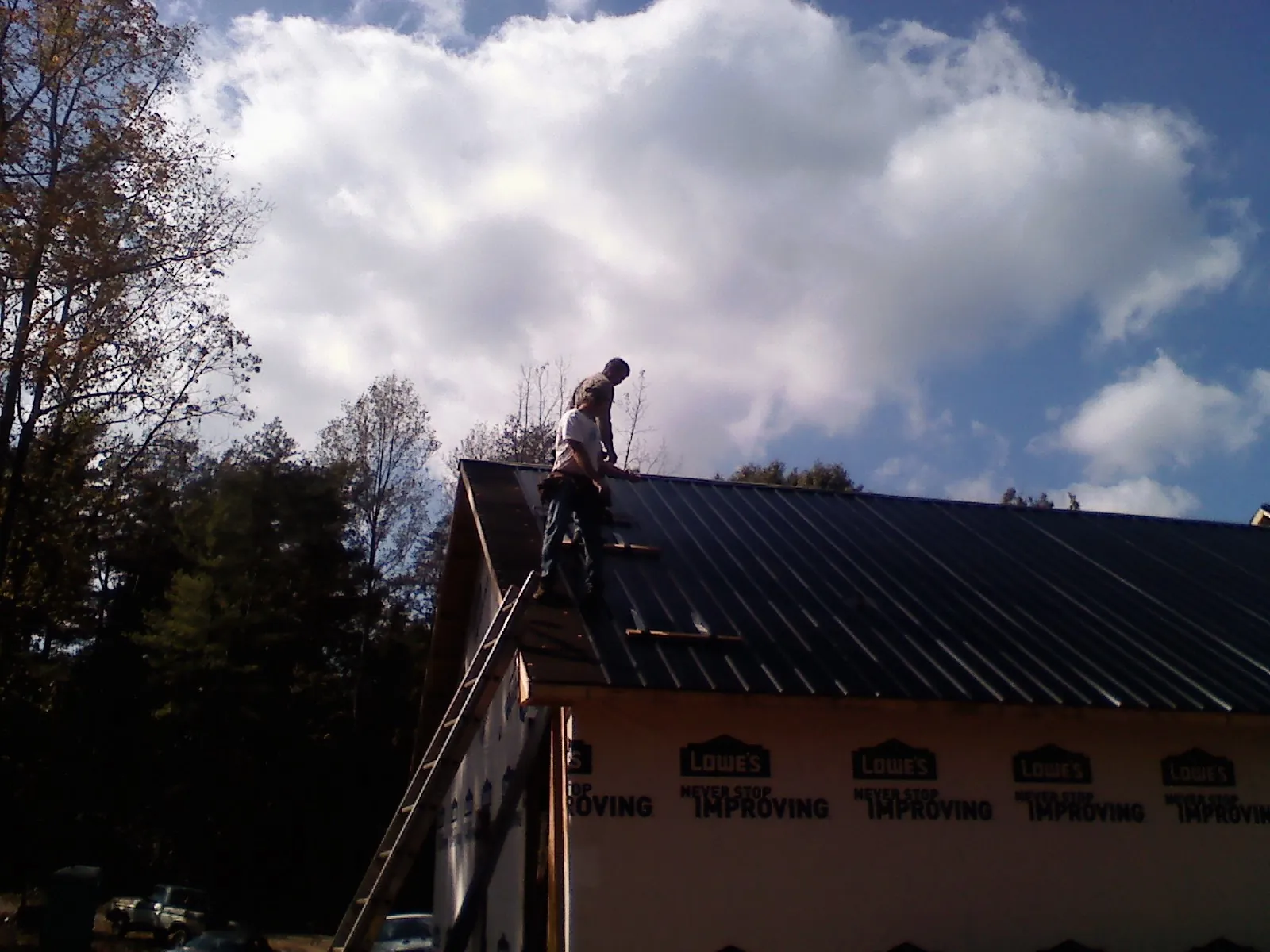 Roofer fastening dark metal panels high against a cloudy sky, from a Roof Inspection job in Pavilion
