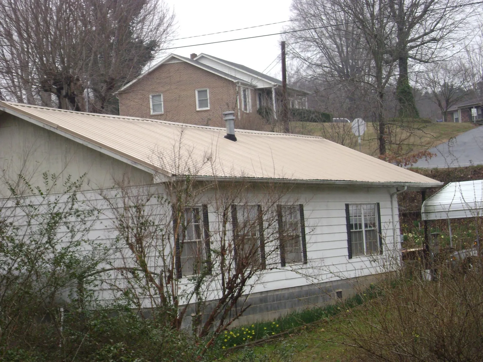 Tan metal roof on a white sided house set into a hillside — Commercial Roofing by Roofing Brothers in Pavilion