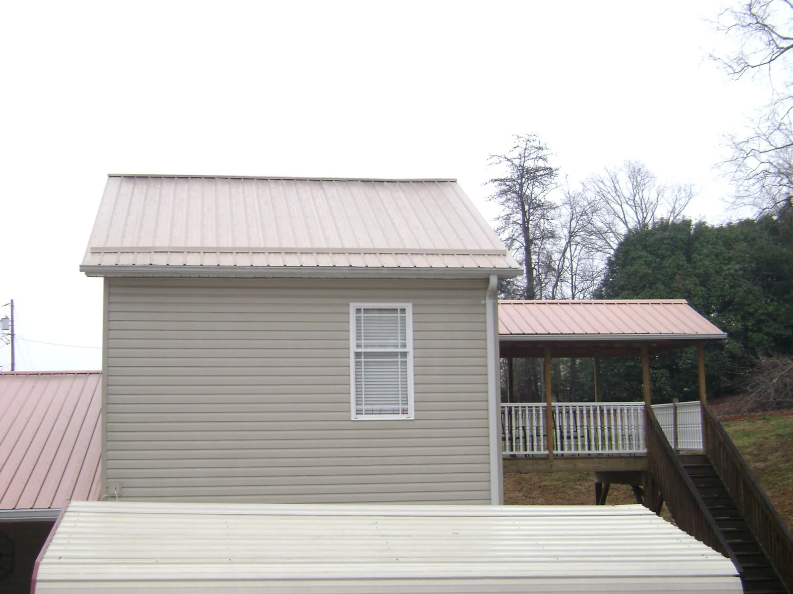 Tan metal roofs on a two story addition and attached porch, from a Roof Replacement job in Pavilion